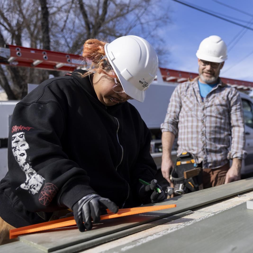  A student marks wood at a construction site while teachers observe